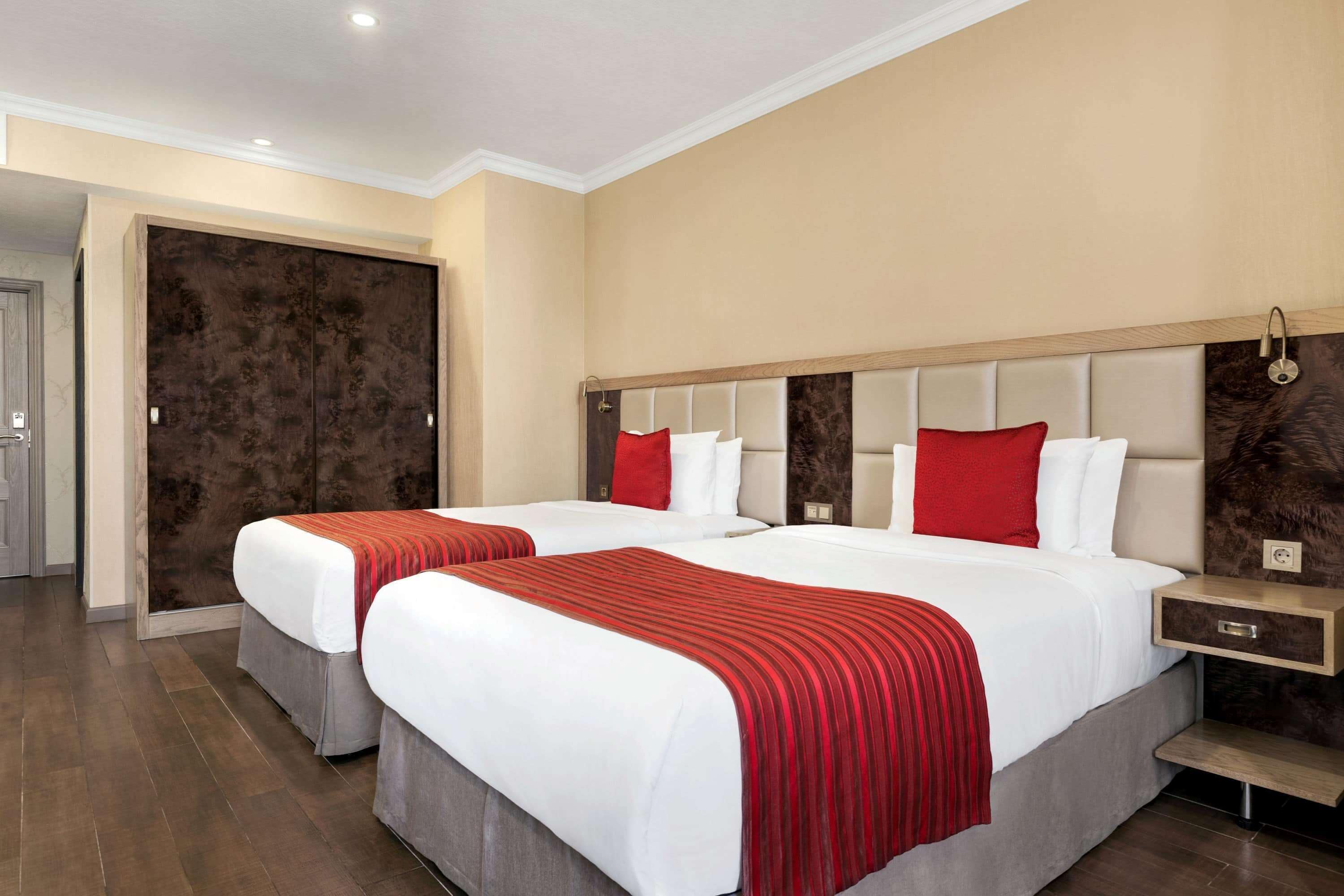 A hotel room with two beds, a large wardrobe, and a nightstand with a lamp.
