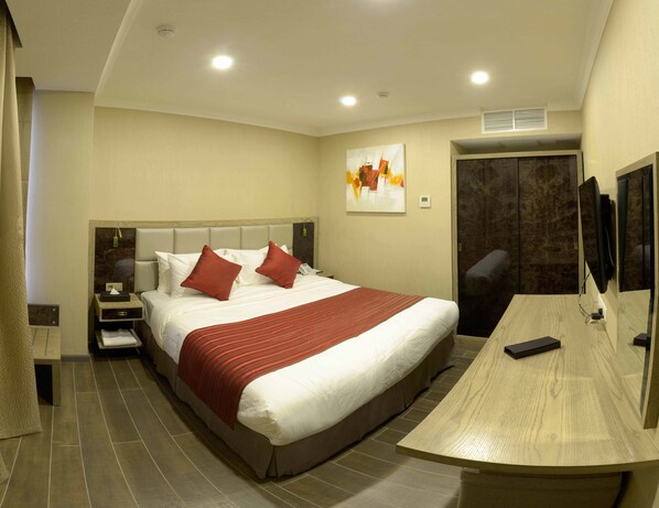 Una habitación de hotel con una cama grande, un escritorio, una silla, un televisor y un armario.