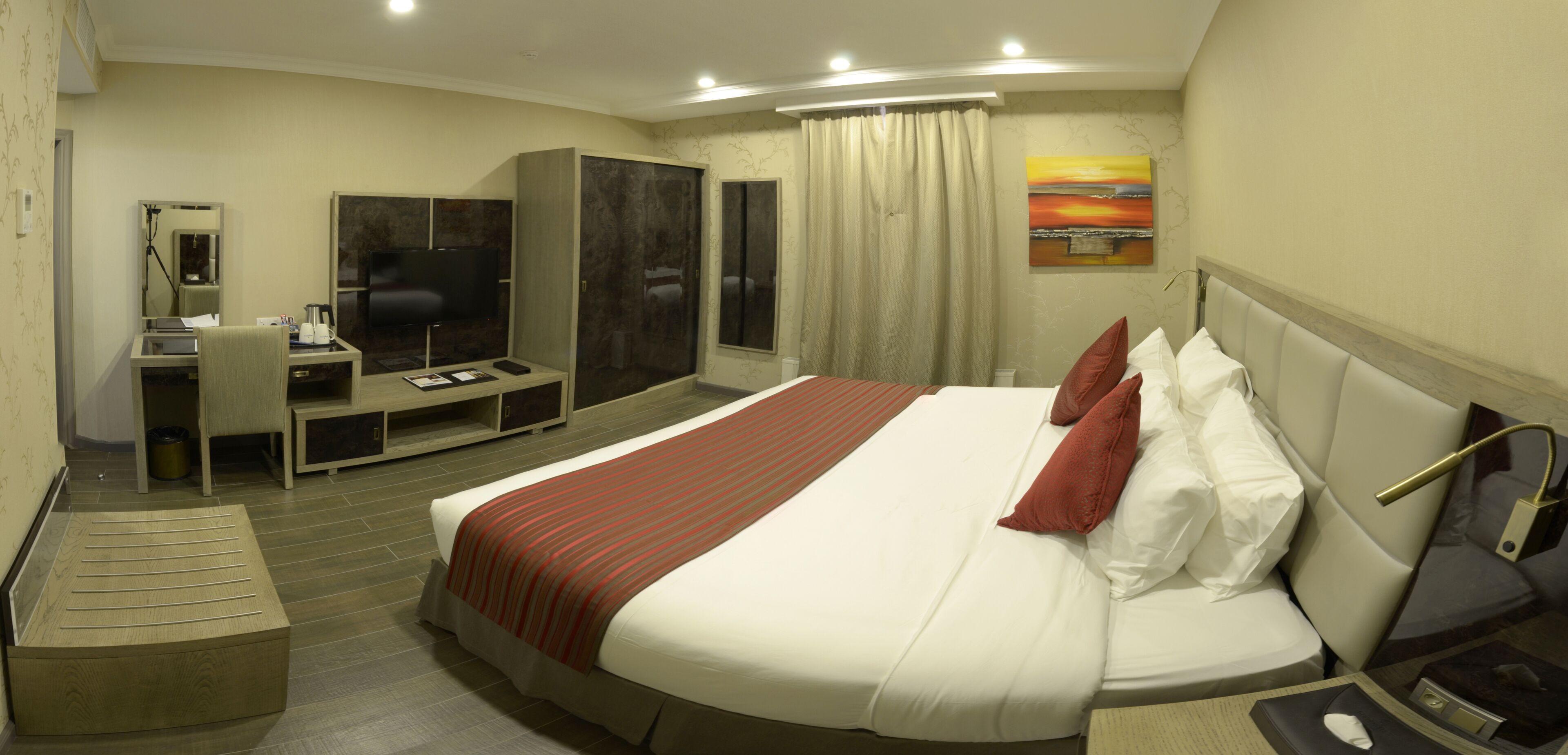 A hotel room with a large bed, a desk with a chair, a wardrobe, and a television.