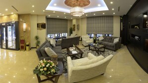 A spacious lobby with a high ceiling, recessed lighting, and a central chandelier. There are multiple seating areas with sofas and armchairs, a coffee table, and a decorative vase with flowers. - Ramada by Wyndham Bishkek Centre (Bishkek)