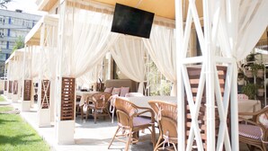 An outdoor seating area with white canopies, wicker furniture, and a flat-screen TV mounted on a pillar. - Ramada by Wyndham Bishkek Centre (Bishkek)