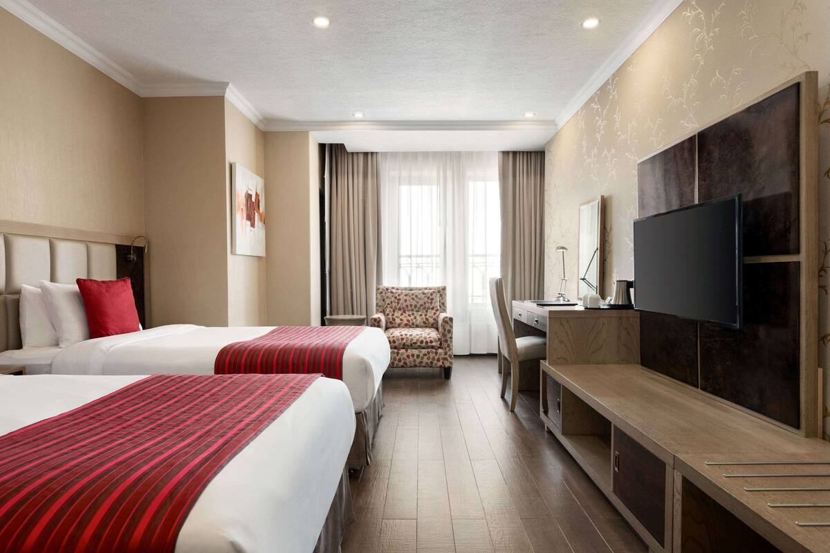 Una habitación de hotel con dos camas, un escritorio, una silla, un televisor y una ventana con cortinas.