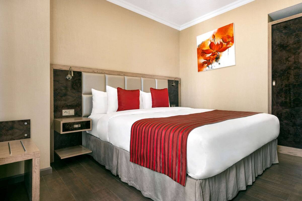 Una habitación de hotel con una cama grande, una mesita de noche, una mesita auxiliar de madera y un cuadro en la pared.