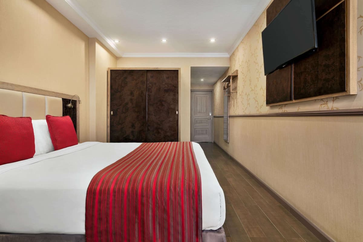 Habitación de hotel con una cama grande, un televisor montado en la pared y una puerta que da a otra habitación.