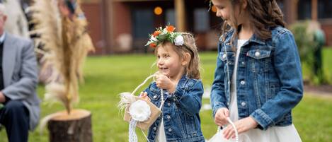 Two children in a grassy outdoor area, one holding a small white box and the other holding a white stringed item.