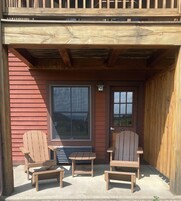 Un porche de madera con dos sillas Adirondack y una mesita.