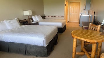 A hotel room with two beds, a wooden table, and a kitchenette.