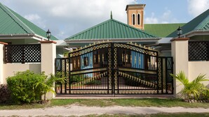 Un ingresso recintato con un cancello decorativo, un edificio con tetto verde e un campanile.