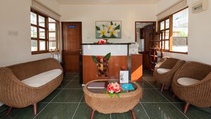 Un'area di accoglienza con una reception in legno, due divani in vimini, un tavolino con un laptop e fiori, e una decorazione a forma di tartaruga sulla parete.