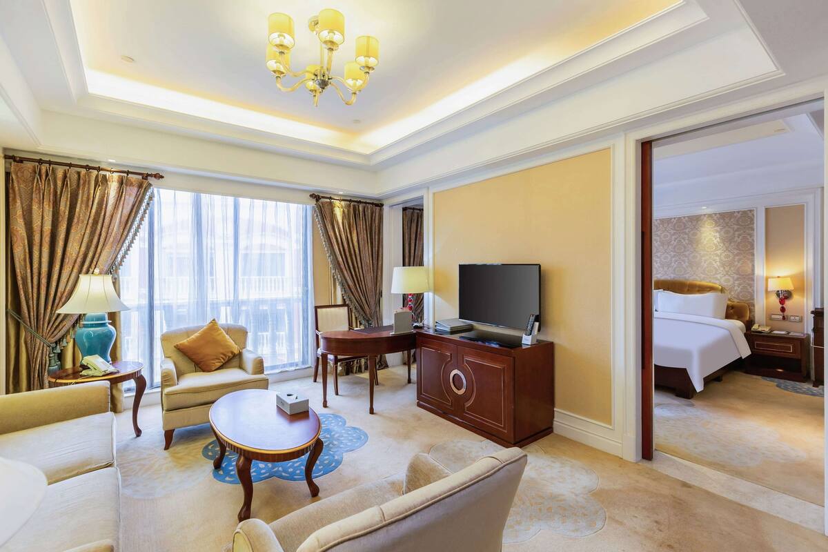 A hotel room with a large bed, a TV, a desk, and a seating area with a sofa and armchairs.