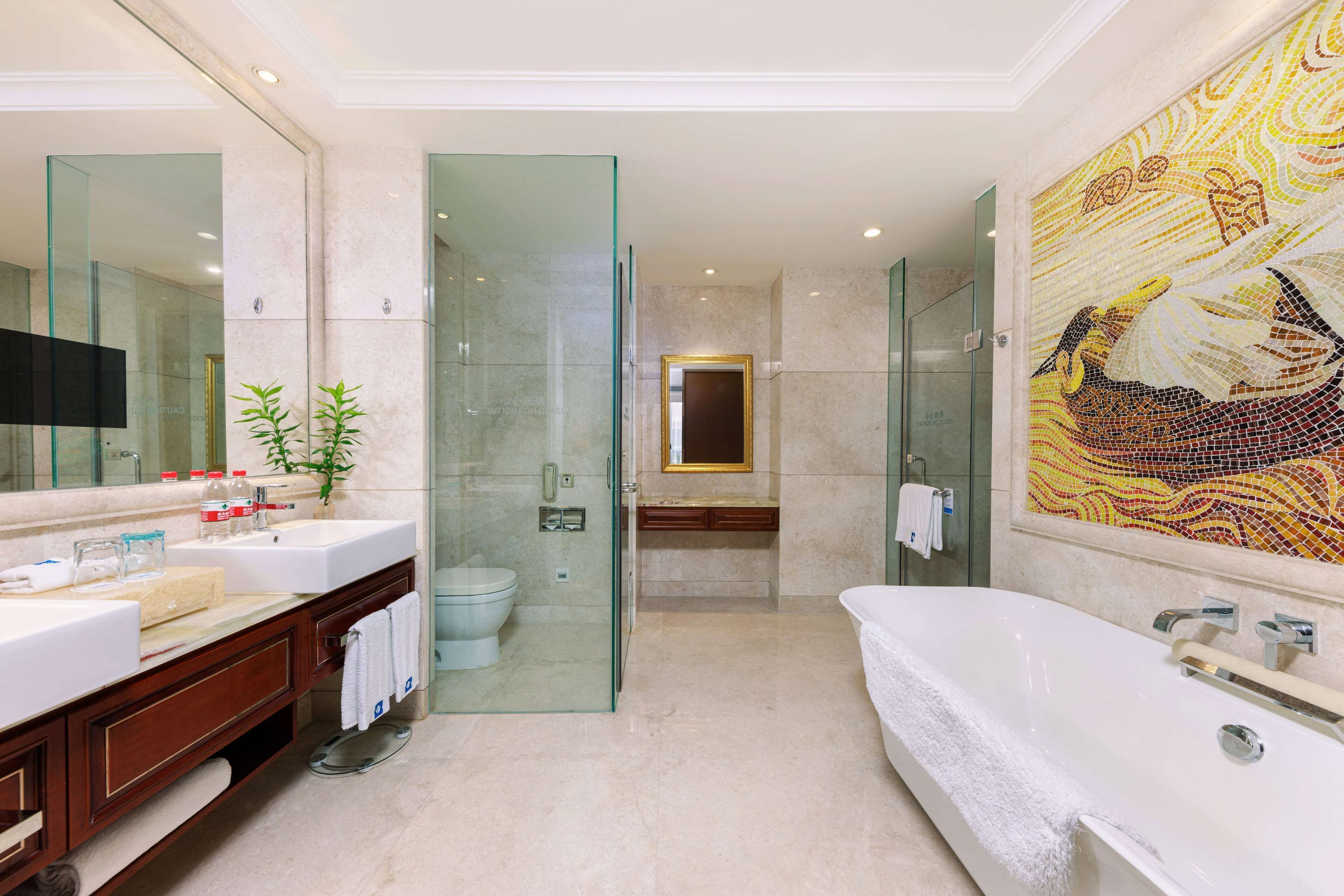 Un baño moderno con ducha de vidrio, una bañera grande y un muro con mosaicos.