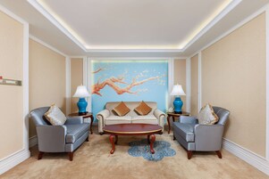 Una habitación con un sofá color beige, dos sillones, una mesa de centro y un mural en la pared.