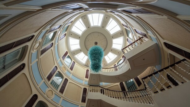 Un atrium à plusieurs niveaux, doté d’une verrière circulaire centrale, d’un escalier en colimaçon et d’un élément décoratif suspendu.