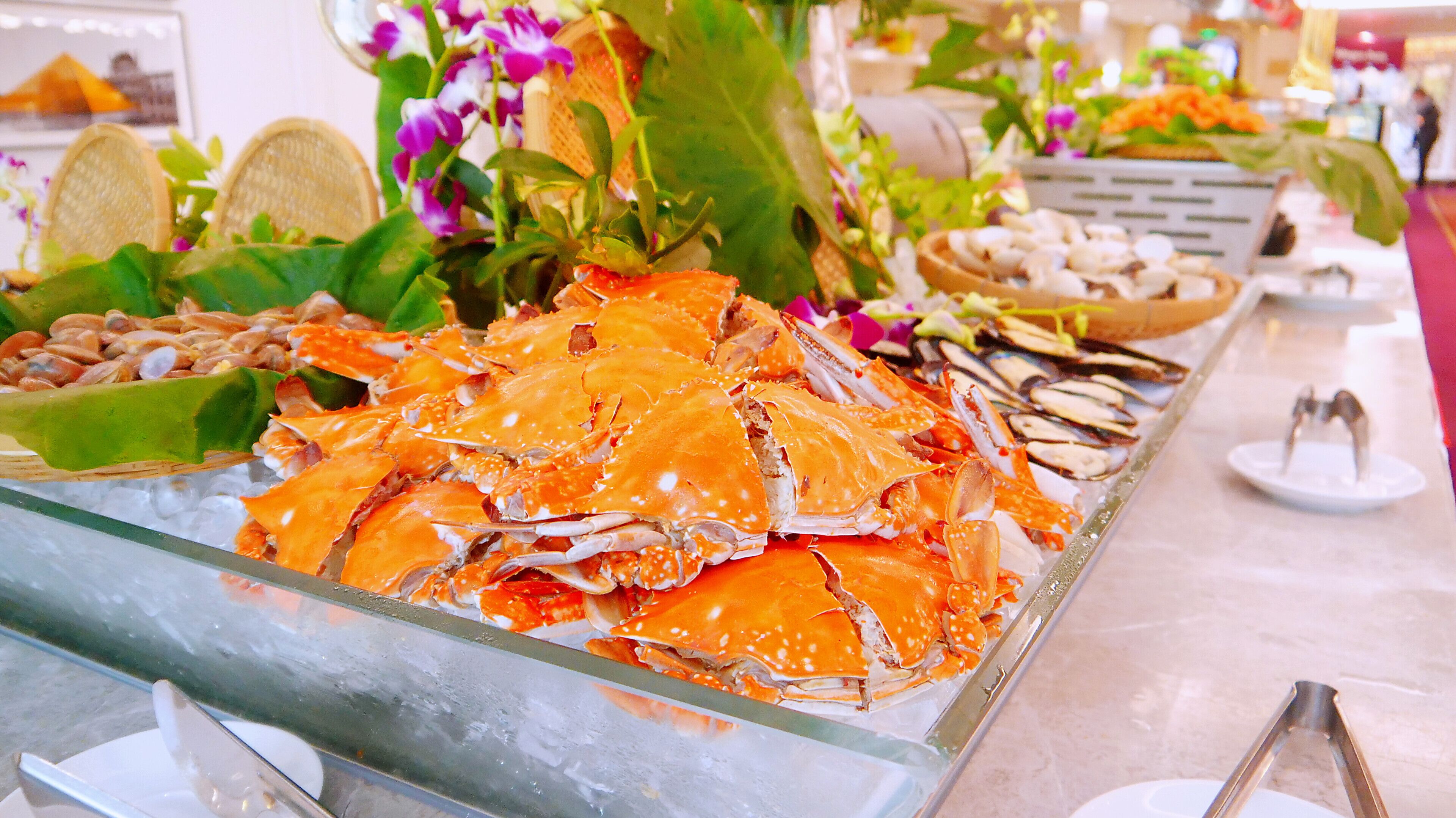 A buffet table with seafood, including crab legs, clams, and mussels, along with some leafy greens and flowers.