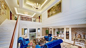 Un vaste salon avec un plafond haut, un escalier et un grand tableau.