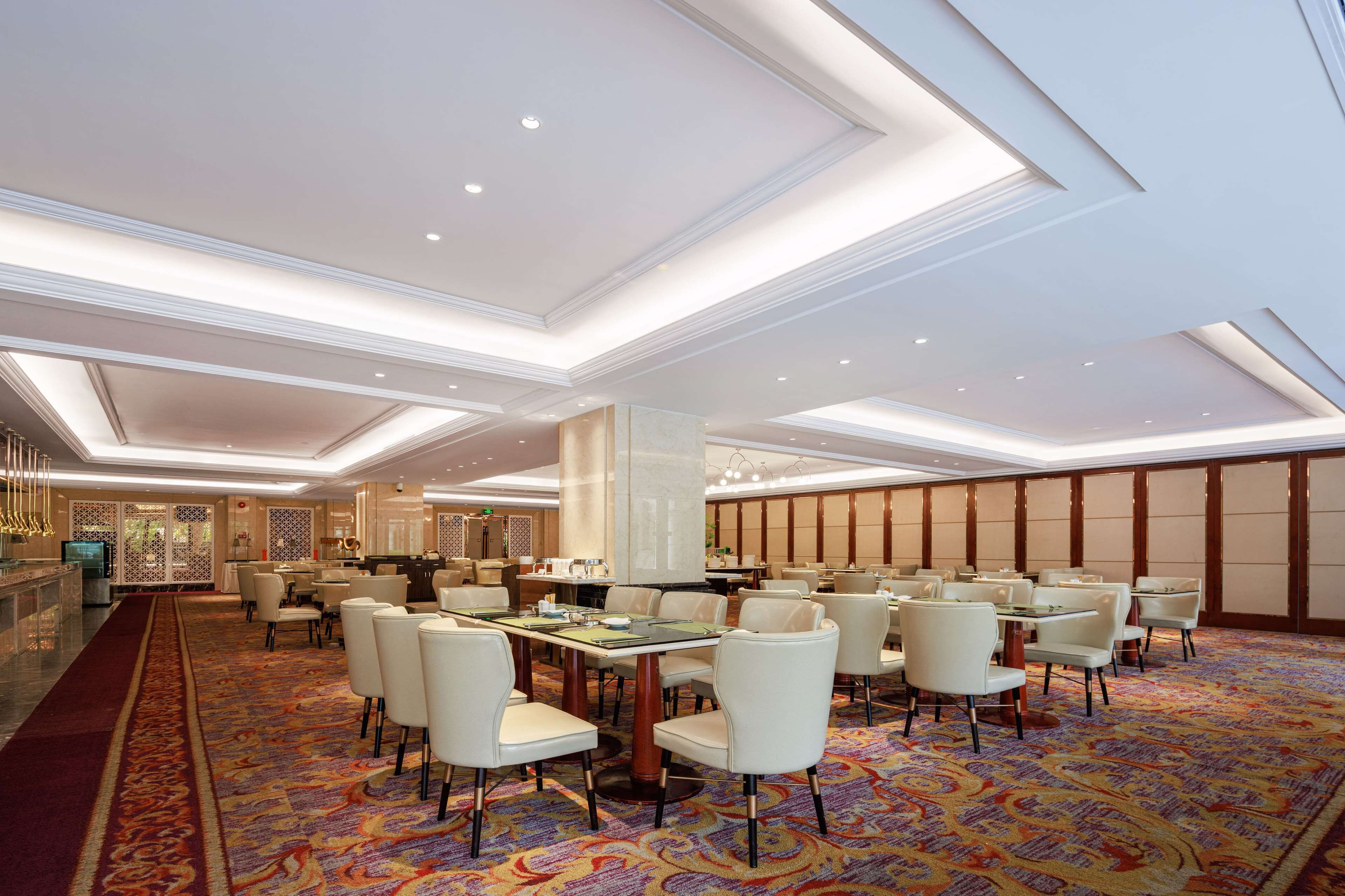 A spacious dining area with high ceilings, recessed lighting, and a patterned carpet.