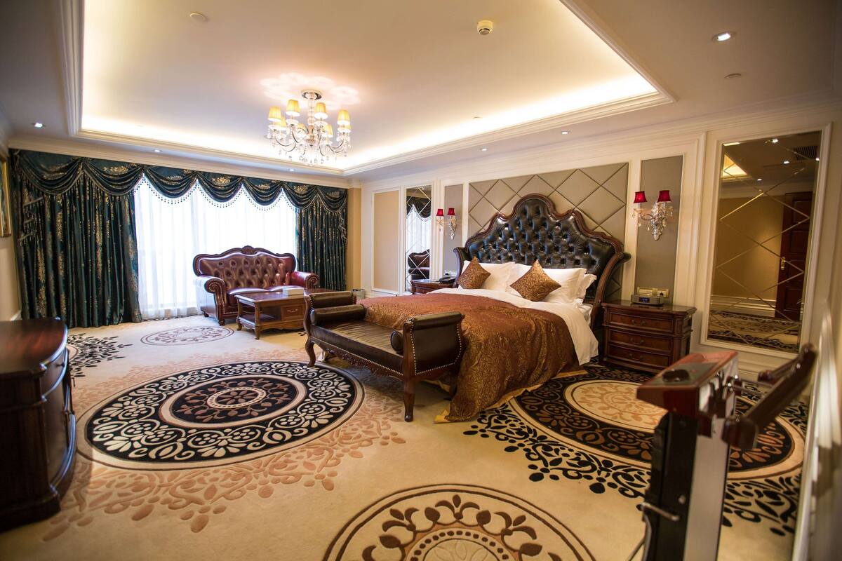 A spacious bedroom with a large bed, a sitting area, and a chandelier.