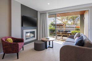 A modern living room with a sofa, armchair, ottoman, and a flat-screen TV mounted on the wall. - Peppers Hunter Valley Accor Vacation Club Apartments (Pokolbin)