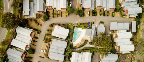 An aerial view of a residential area with multiple detached houses, roads, and a swimming pool.