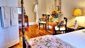 A bedroom with a four-poster bed, wooden furniture, a table with chairs, and a bedside lamp. - The York House Inn (Rabun Gap)