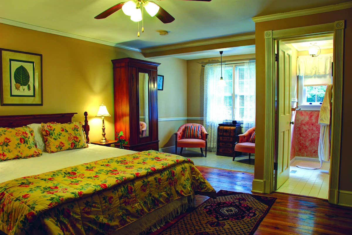 A bedroom with a large bed, a wooden wardrobe, a chair, and a door leading to a balcony.