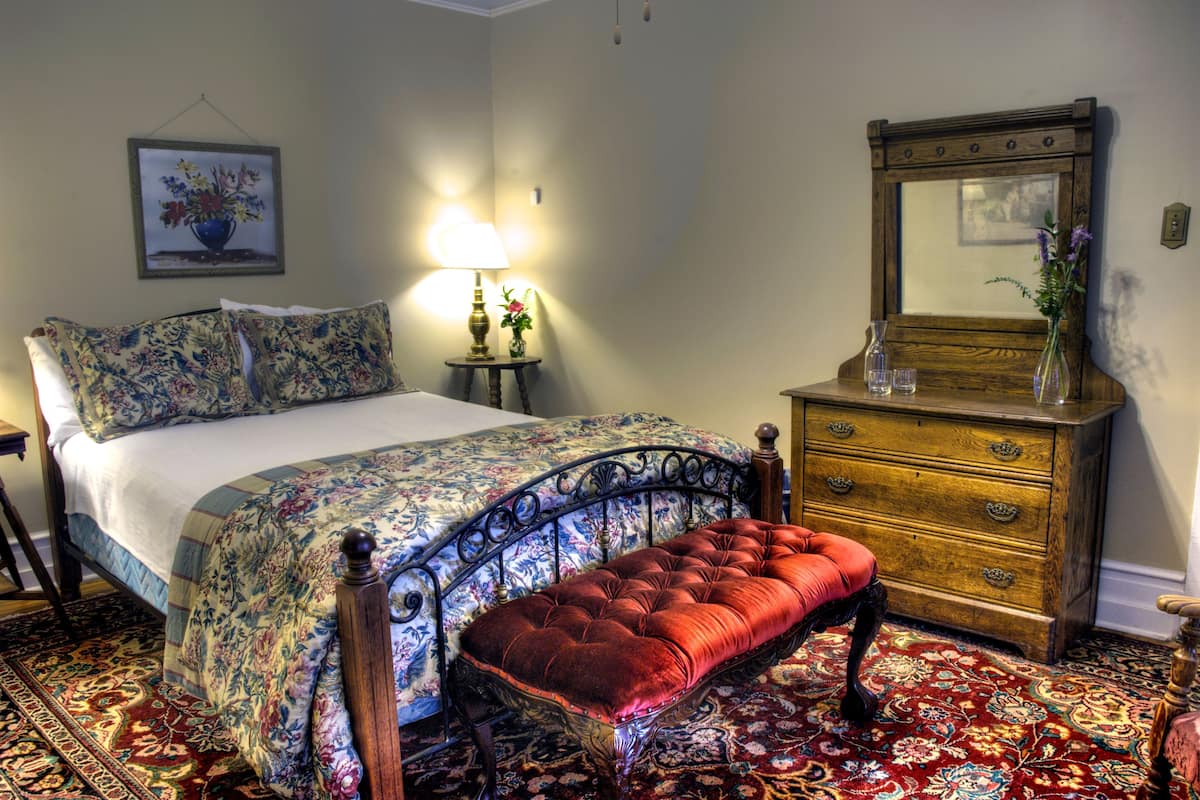 A bedroom with a bed, a bench, a dresser, a lamp, and a mirror.
