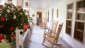 A covered porch with white railings and wooden rocking chairs. - The York House Inn (Rabun Gap)