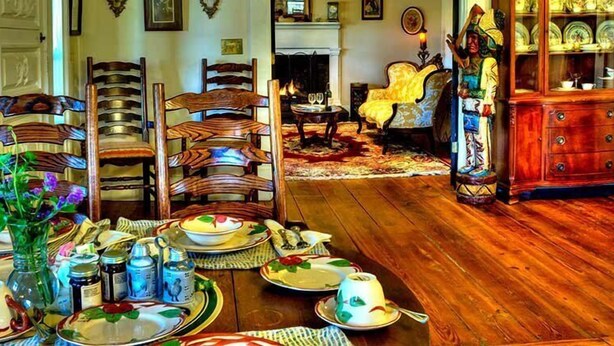 A dining room with wooden chairs, a dining table set with plates, glasses, and a vase of flowers. - The York House Inn (Rabun Gap)
