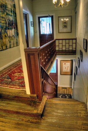 Una escalera de madera con un tapete rojo que lleva a un rellano en el segundo piso.