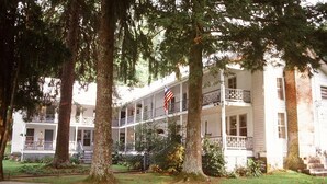 A two-story building with a balcony on the second floor, surrounded by trees and a flag. - The York House Inn (Rabun Gap)