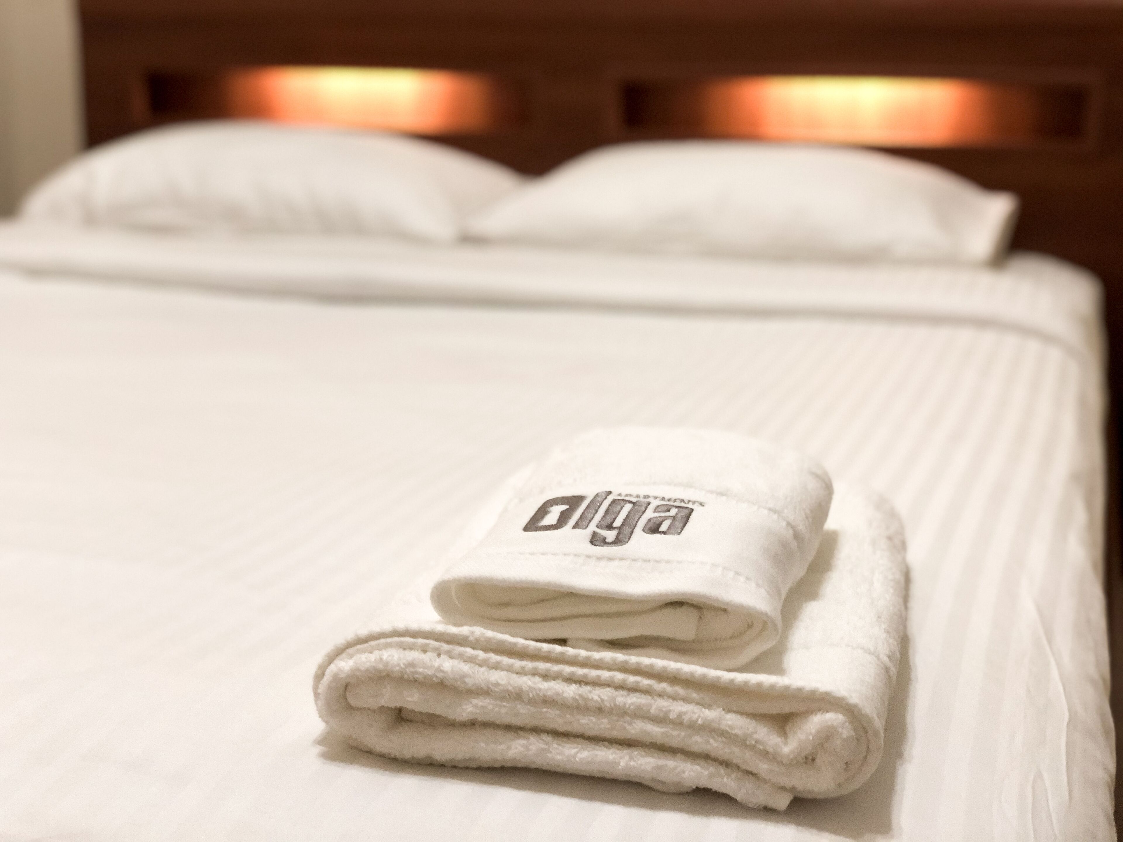 Una cama bien hecha con una toalla blanca doblada encima, un cabecero de madera y una almohada.