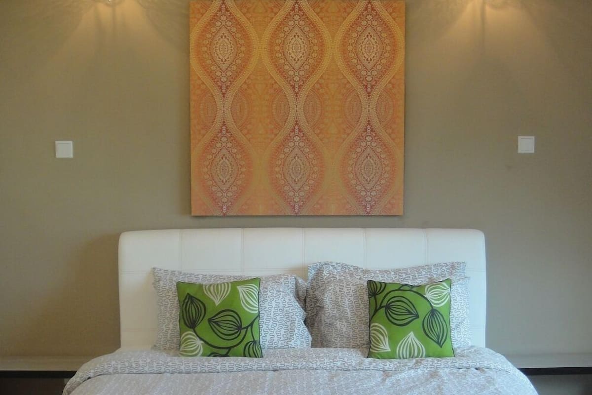 A neatly made bed with patterned bedding, two pillows with leaf designs, and a folded towel on the bed.