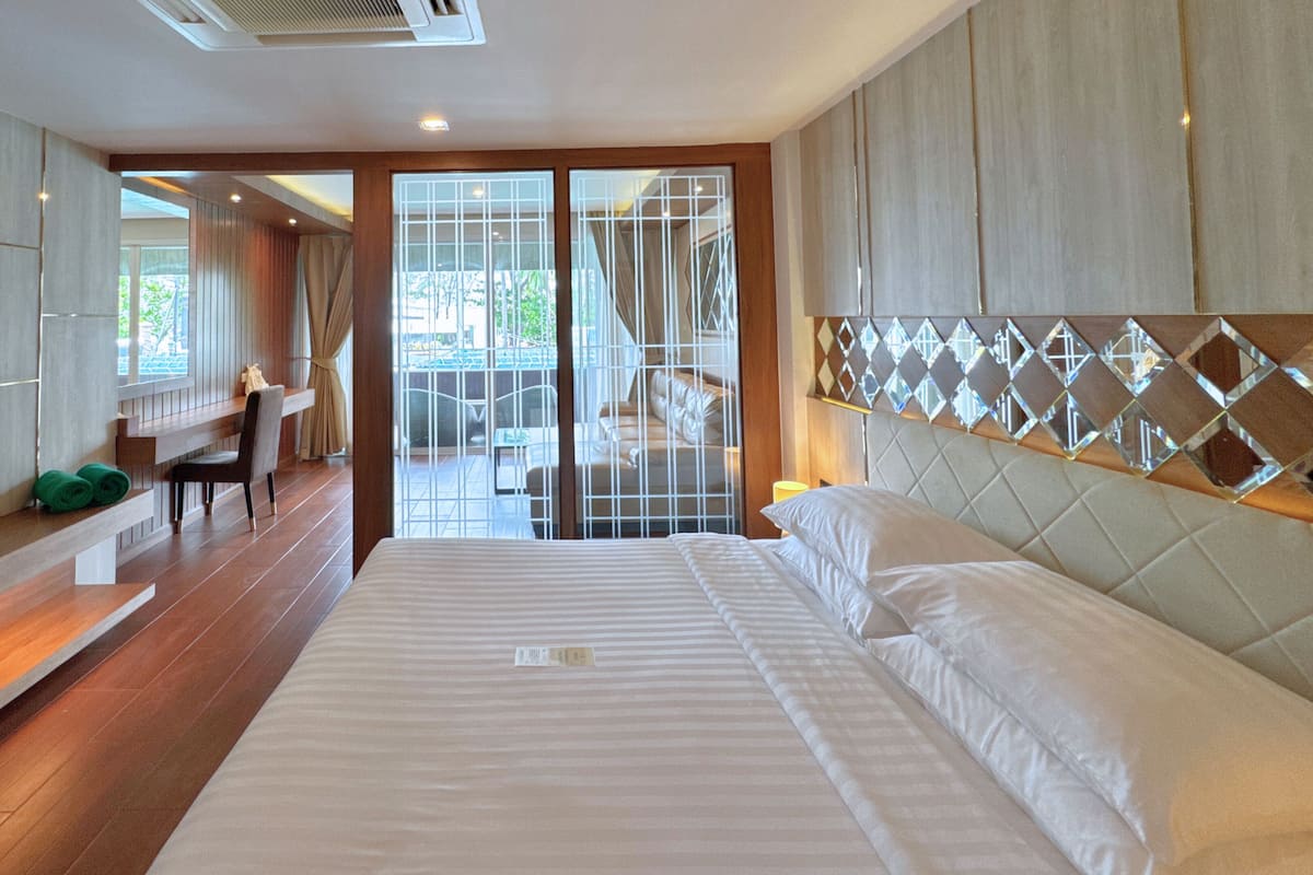 A modern hotel room with a large bed, a flat-screen TV, a desk with a chair, and a view of the outdoors through a glass door.