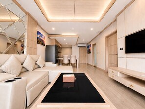 A modern living room with a sofa, a coffee table, a TV, and a kitchen area in the background.