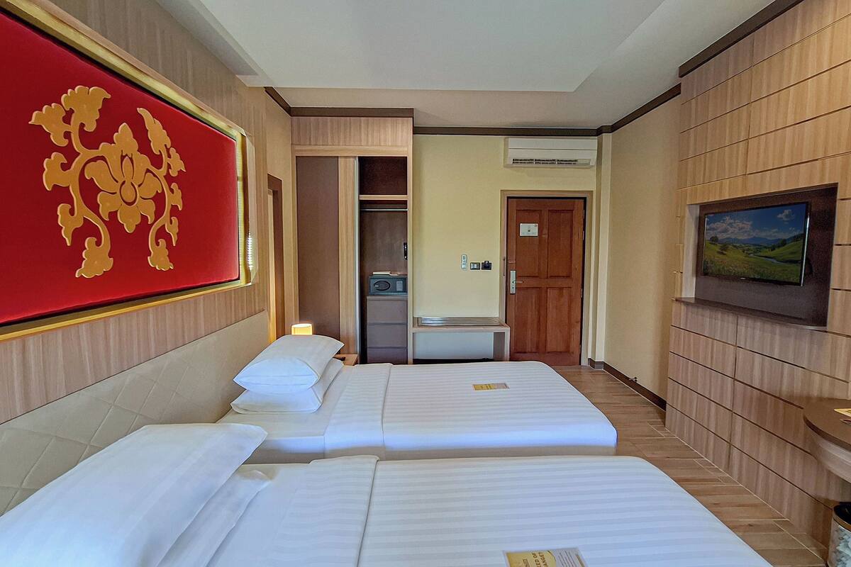 A hotel room with two beds, a red decorative wall, a television, and a small bathroom.