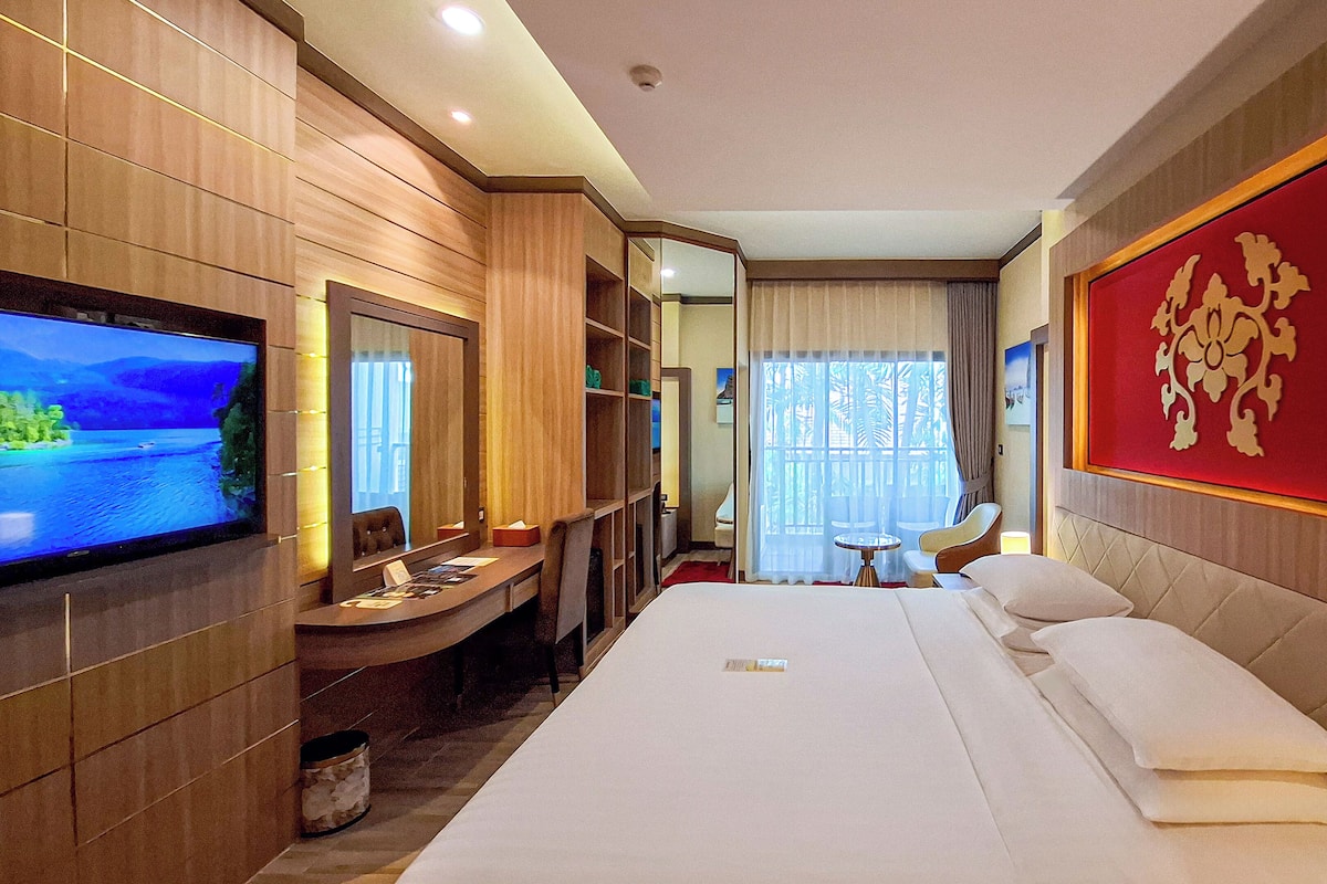 A hotel room with a large bed, a TV, a desk, and a red decorative wall piece.