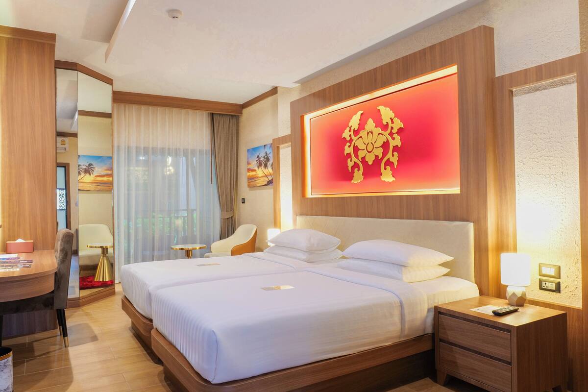 A hotel room with a large bed, a desk with a TV, a chair, and a wall with a decorative emblem.