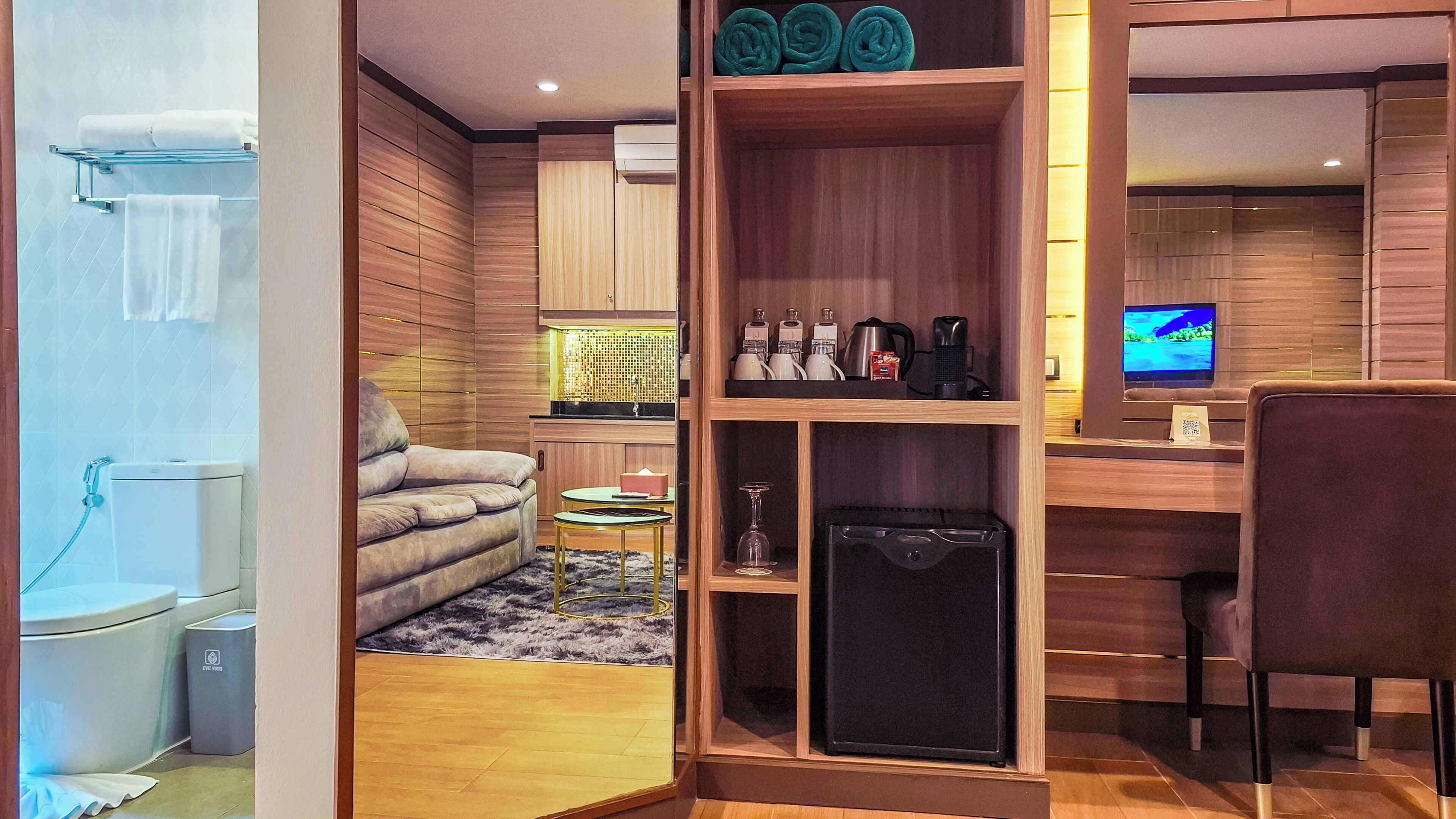 A modern hotel room with a sofa, a small table, a TV, and a cabinet with toiletries.