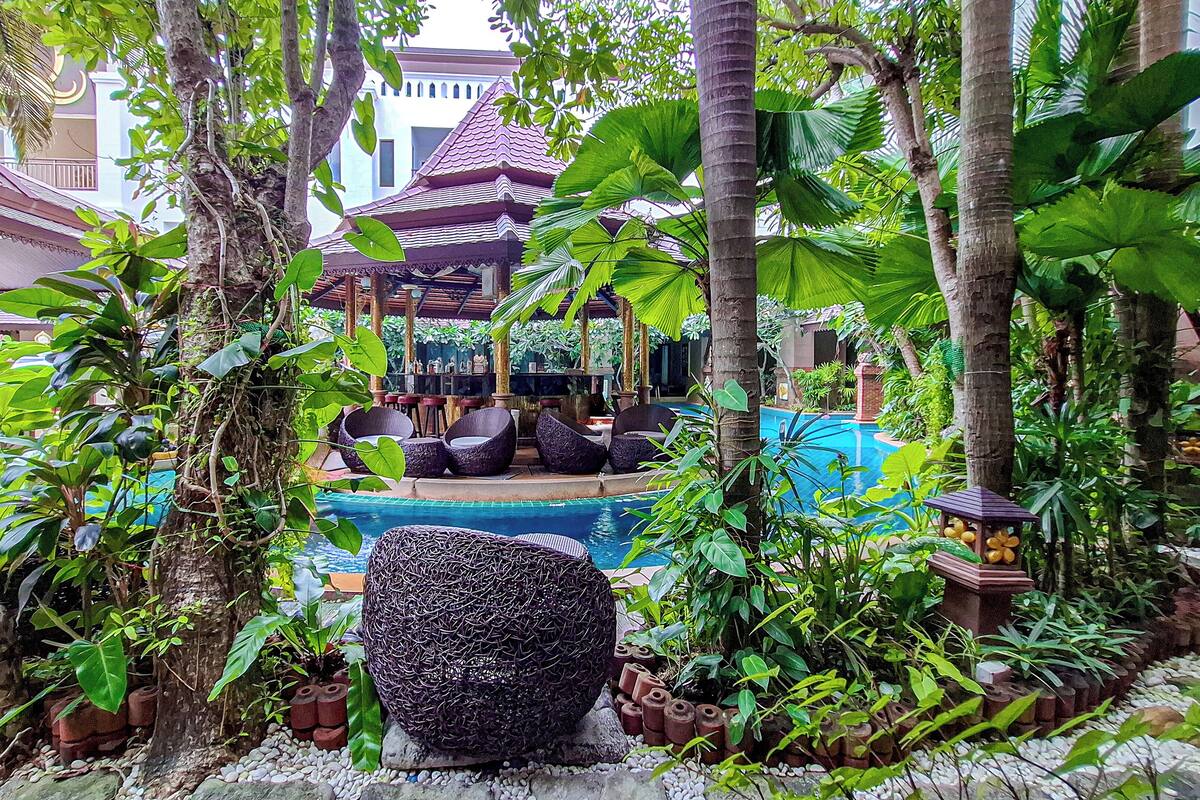 A pool area surrounded by lush greenery, with a traditional pavilion and seating arrangements.