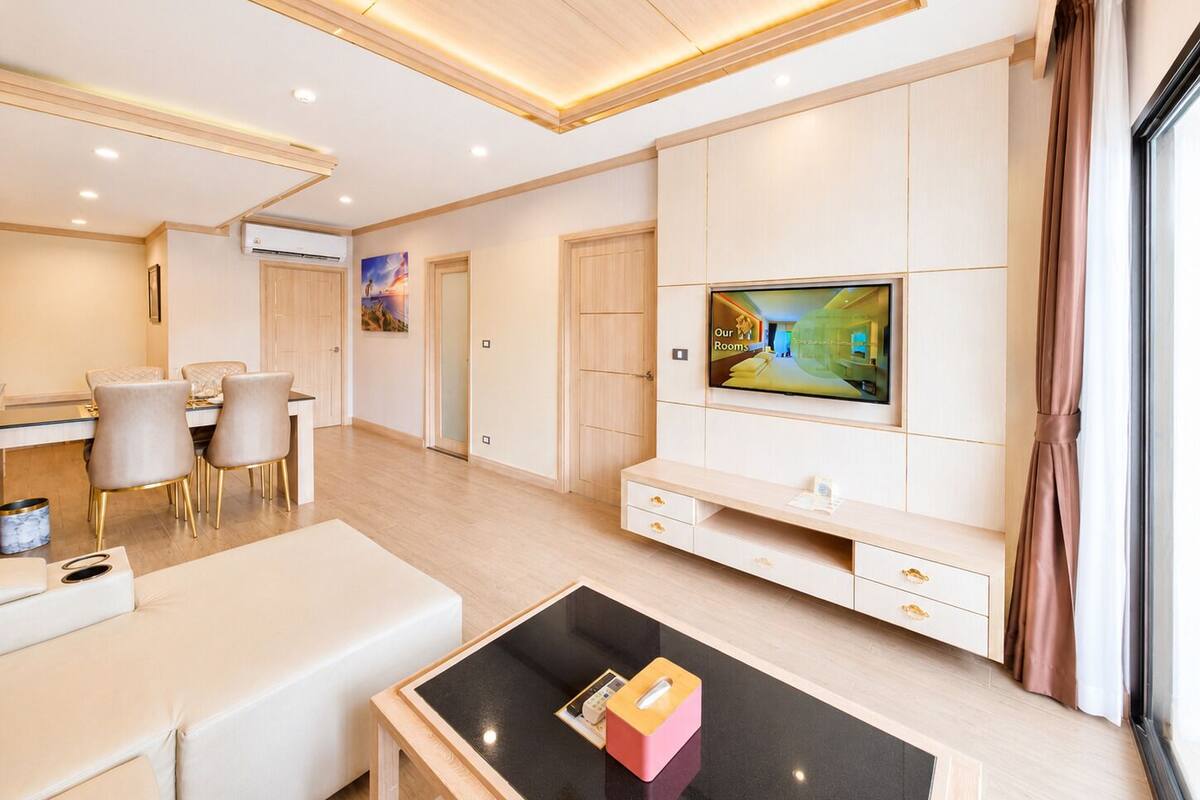 A modern living room with a flat-screen TV, a sofa, a coffee table, and a dining area with chairs.