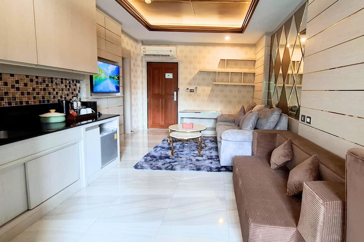 A modern kitchen with a TV, a dining area with a sofa and a coffee table, and a living room with a patterned wall and a ceiling light fixture.