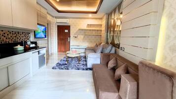 Una cocina moderna con televisor, un comedor con sofá y mesa de centro, y una sala de estar con pared estampada y lámpara en el techo.