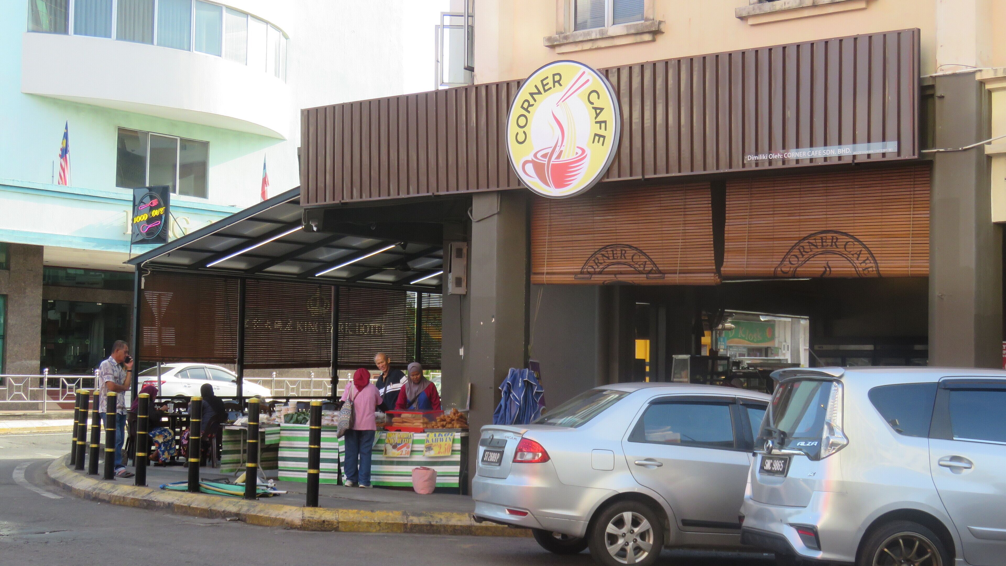 Un café de esquina con un llamativo letrero amarillo que muestra una ilustración de fideos.