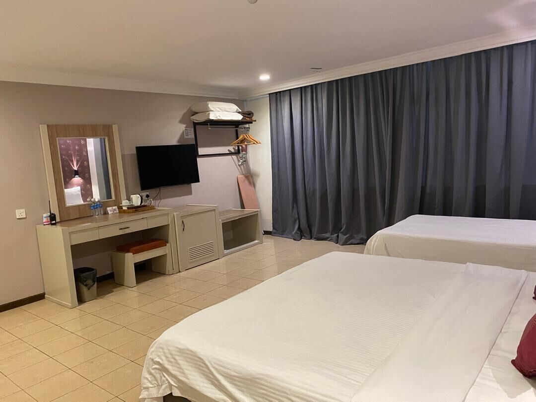 A hotel room with two beds, a desk with a TV, and a large window with curtains.