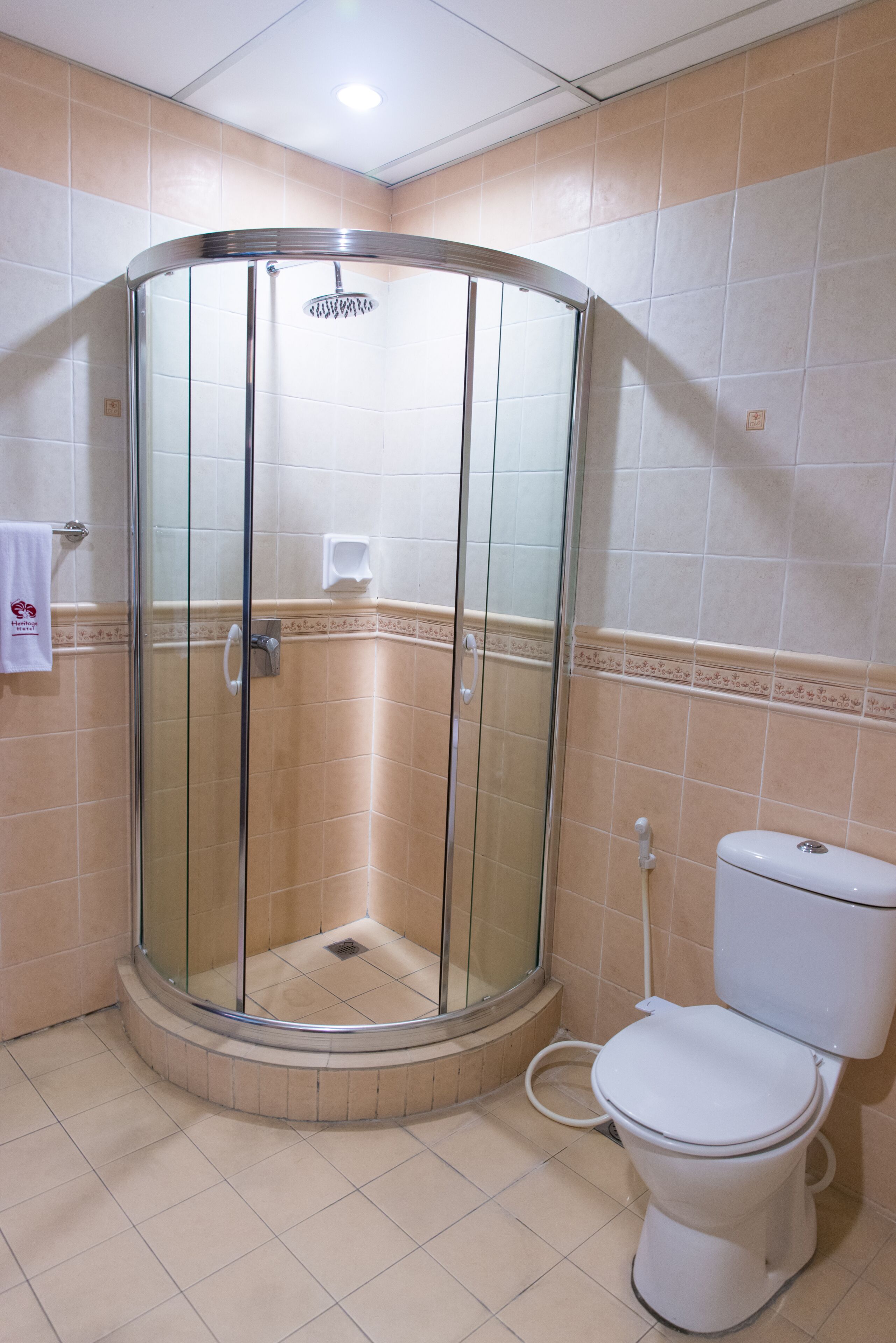 A bathroom with a glass-enclosed shower, a toilet, and beige tiled walls.