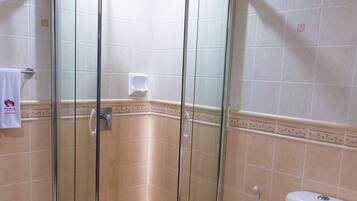 A bathroom with a glass-enclosed shower, a toilet, and beige tiled walls.