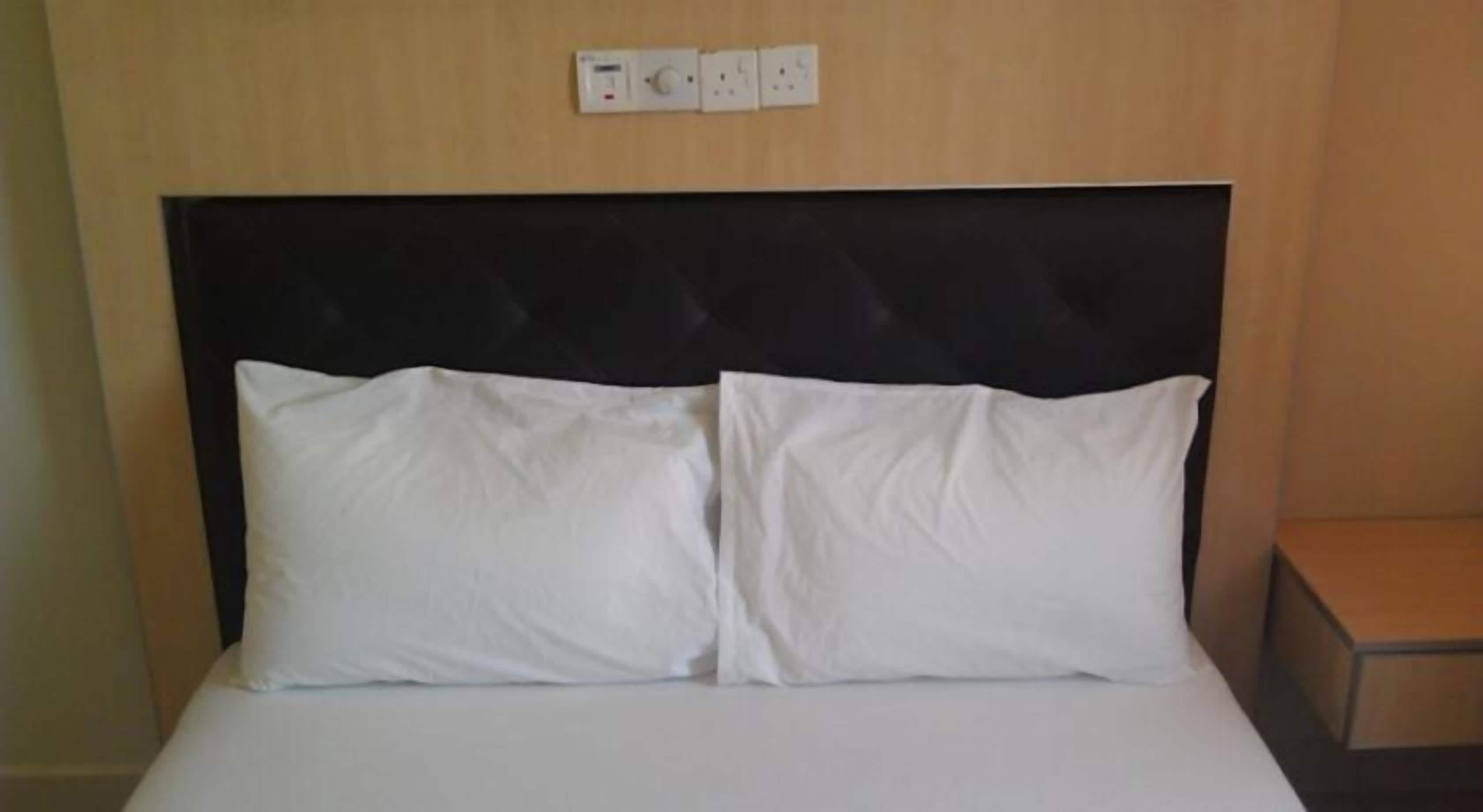 Un lit avec du linge de lit blanc et une tête de lit noire, dans une chambre d’hôtel.