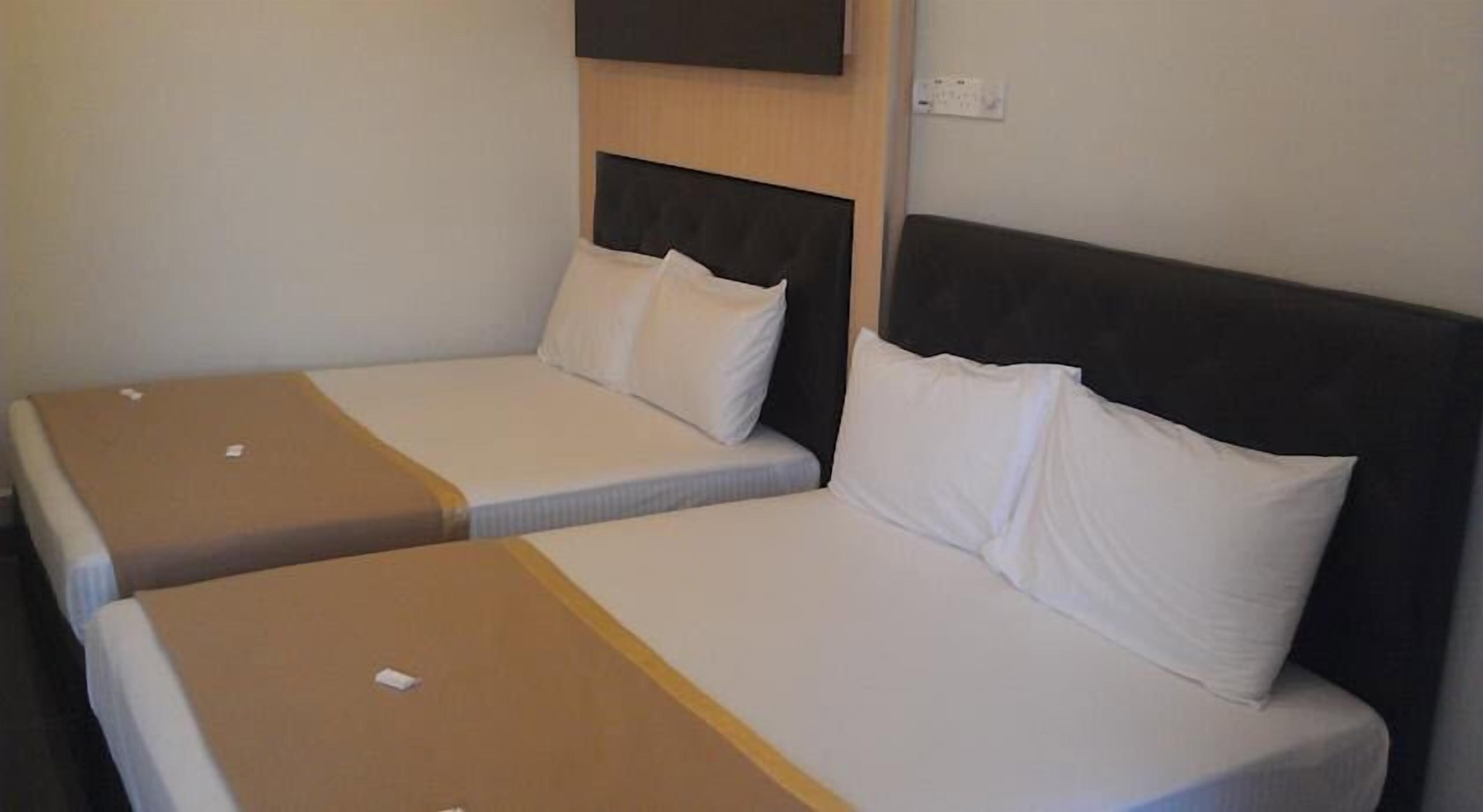 Deux lits simples avec des têtes de lit, un panneau en bois au-dessus, et une horloge fixée au mur.