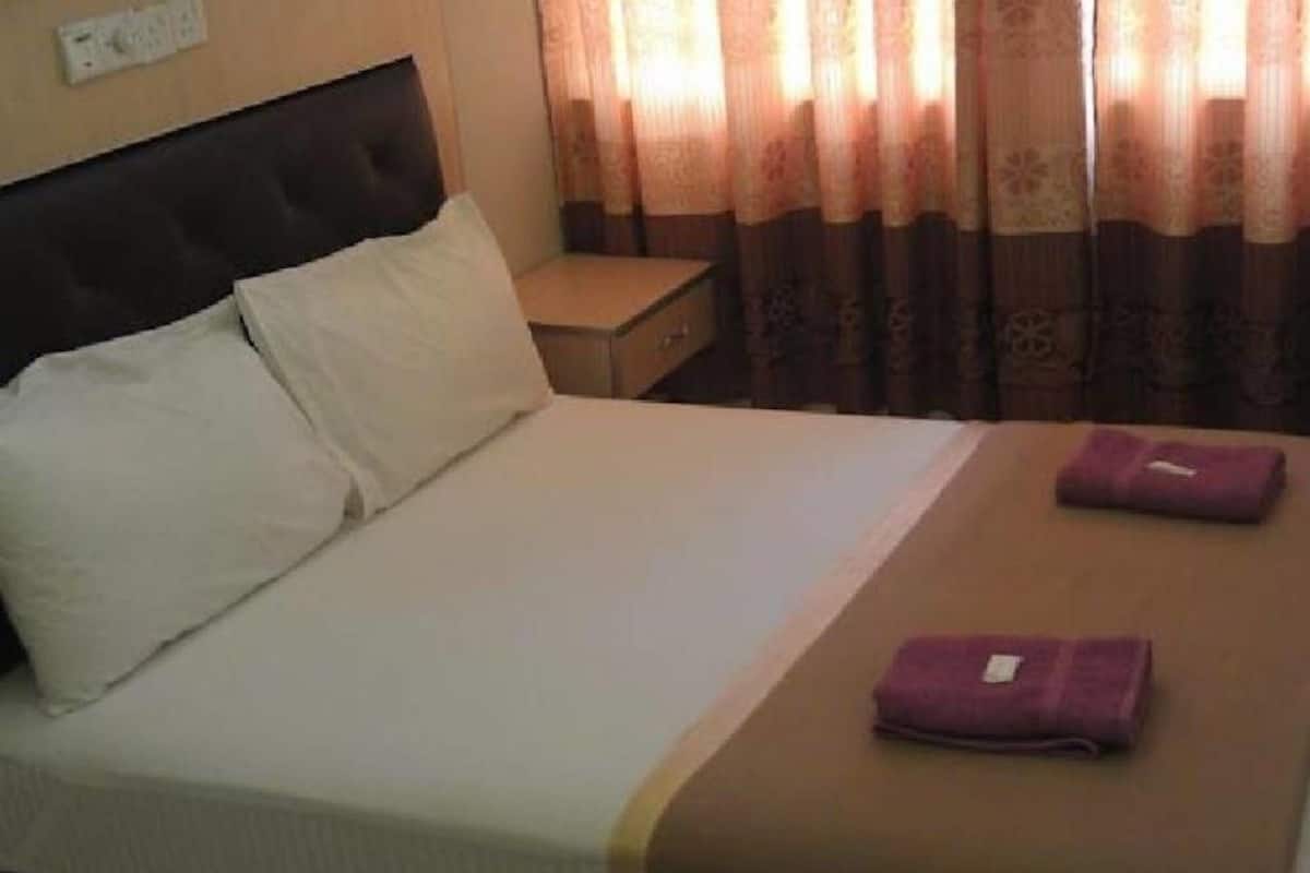 A neatly made bed with white and brown linens, a small bedside table, and a purple towel on the bed.