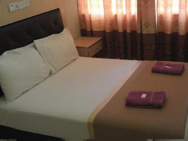 A neatly made bed with white and brown linens, a small bedside table, and a purple towel on the bed. - Serdang Business Hotel (Seri Kembangan)